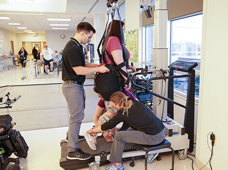 Patient receiving spinal cord rehabilitation with a therapist using assistive technology