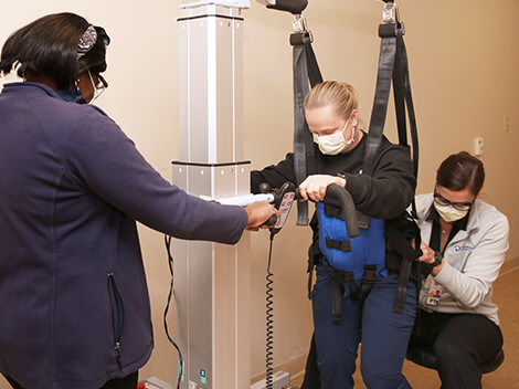 Female patient being fit into overhead safety harness.