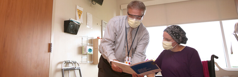 Doctor leaning down to show female patient test results in her hospital room.