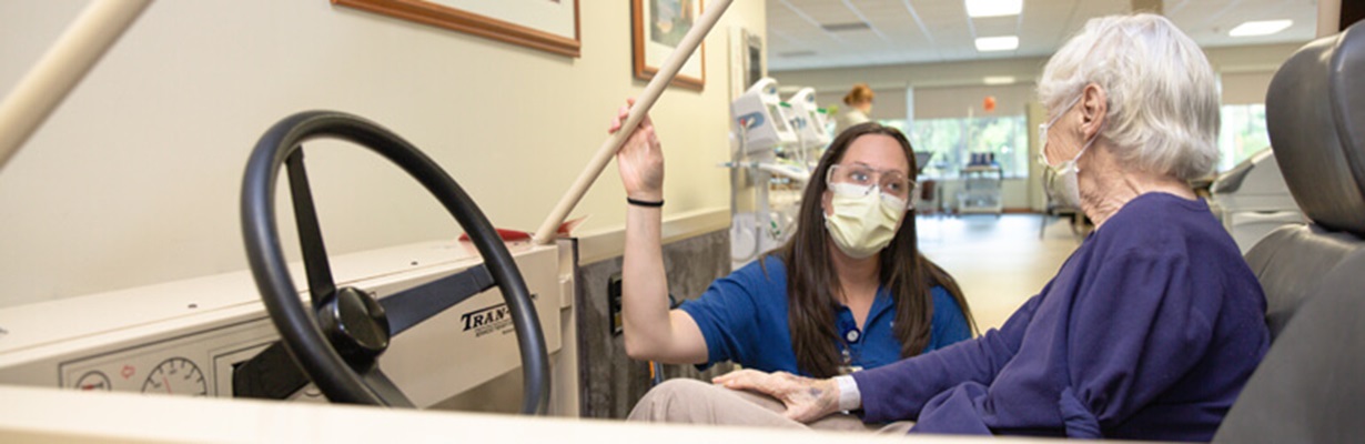 Senior female patient sitting in simulated car talking to therapist.