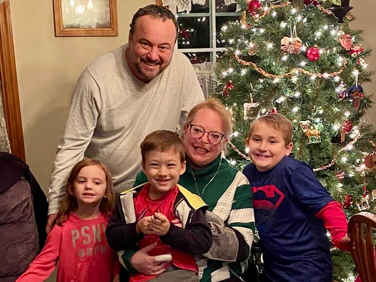 Julie and her family in front of decorated Christmas tree with lights.
