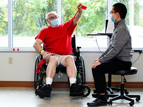 Male patient wearing red shirt holding a red block in his raised hand.