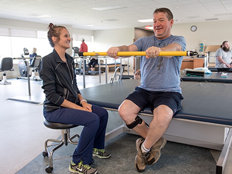 Male patient holding therapy stretching and balance stick in outstretched arms.