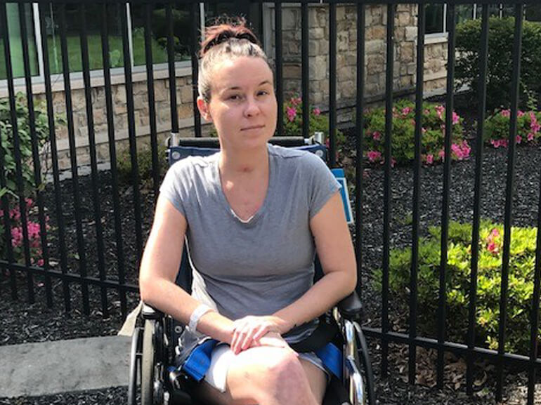 Heather sitting outside in a wheelchair on a sunny day in front of a garden.