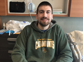 Zach wearing green hoodie while sitting in hospital room  and smiling