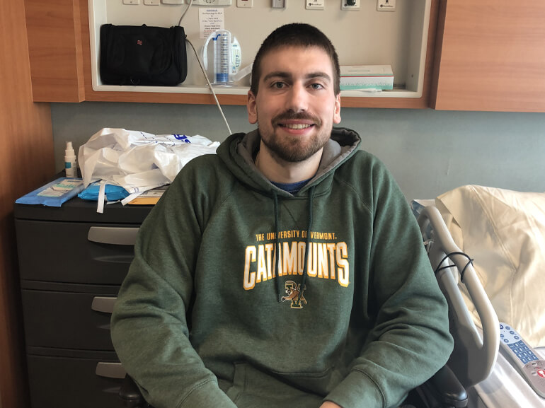 Zach wearing a dull green pull-over hoodie and sitting next to his hospital bed.