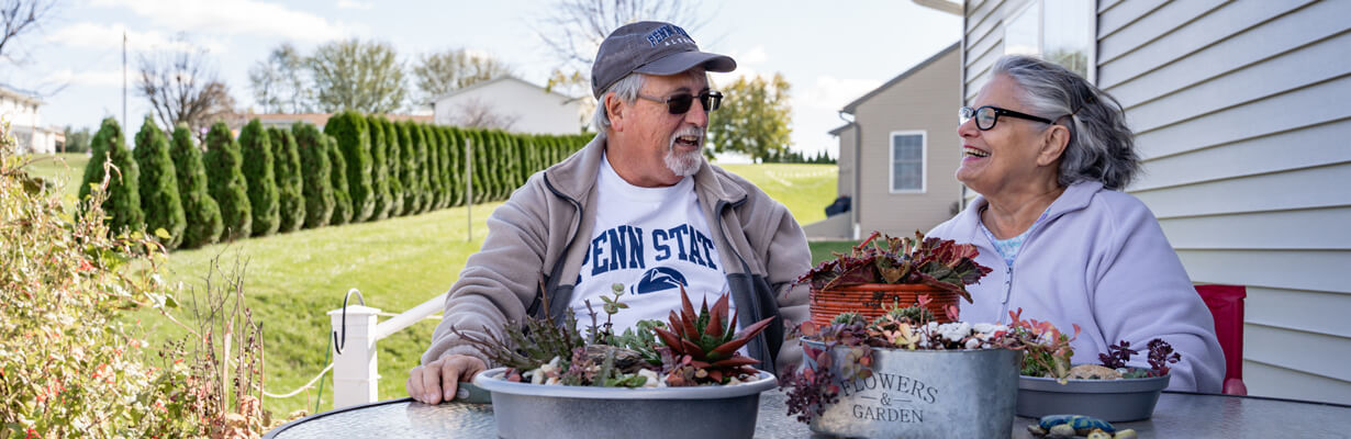 Senior man in Penn State shirt siting with senior female outside at a table on a backyard deck.