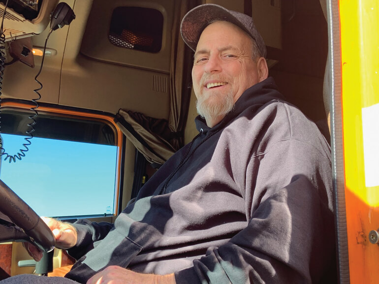 Wayne sitting in the cab of his truck with the door open, smiling.