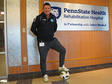 Denis with one foot resting on a soccer ball, standing in hospital hallway.