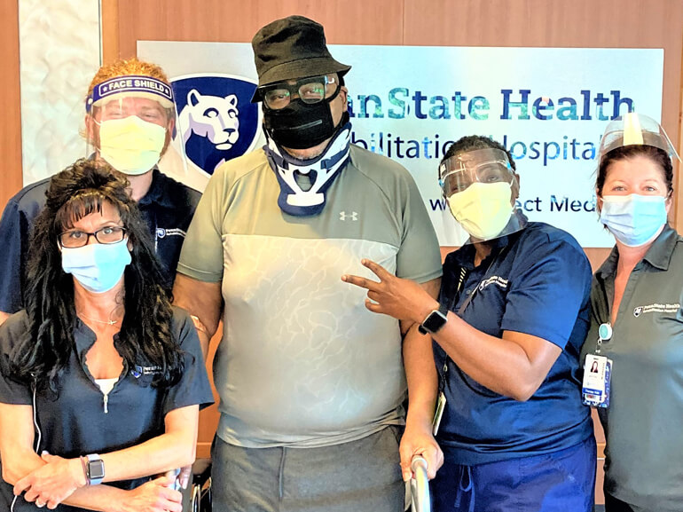 Nate wearing a Covid 19 mask and a neck brace, standing with a group of therapists.
