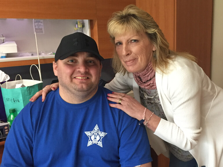 Kevin wearing a blue t-shirt with the state corrections logo and his mom in his hospital room.