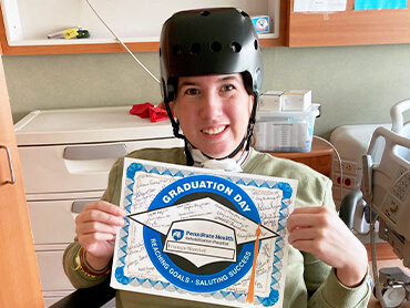 Frances wearing a protective helmet and holding a certificate marking her discharge from the hospital.