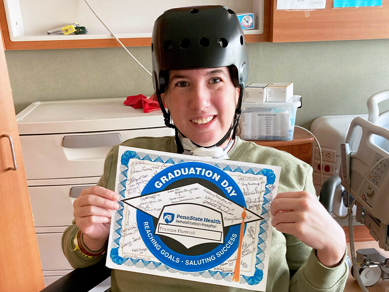 Fran wearing a protective helmet and holding a certificate marking her discharge from the hospital.