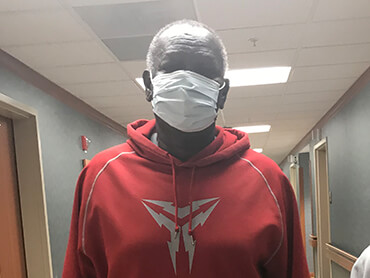 Gordon wearing a red jacket and Covid mask standing in a hospital hallway.
