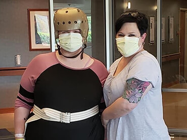 Kayla wearing a cranial helmet and standing beside a female therapist.