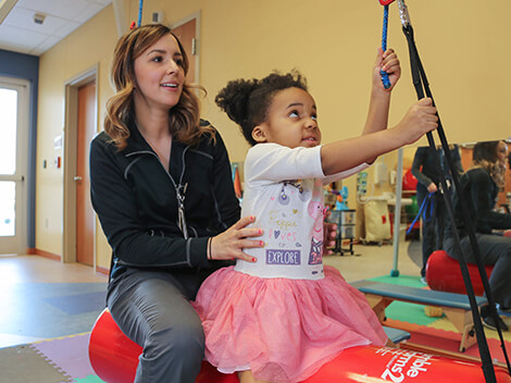 Female therapist helps small girl use an arm pulley.
