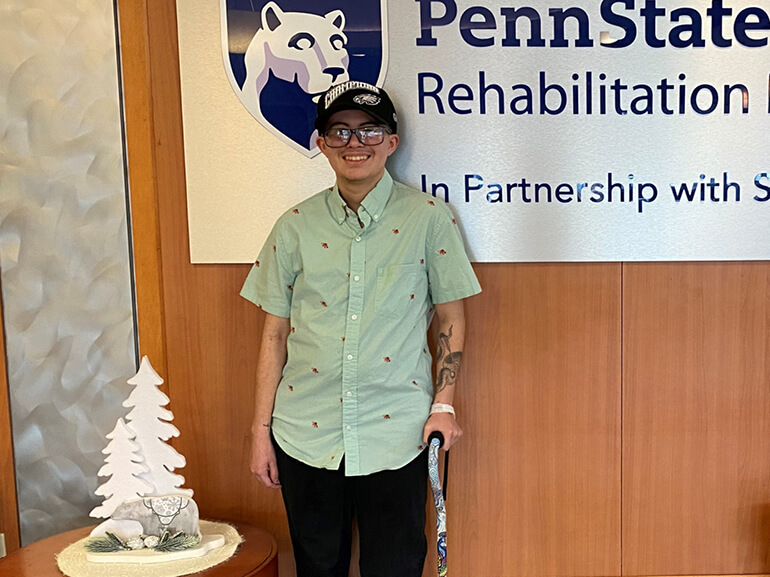 Leo Hernandez leans on a cane and stands next to a Penn State Rehabilitation Hospital sign.